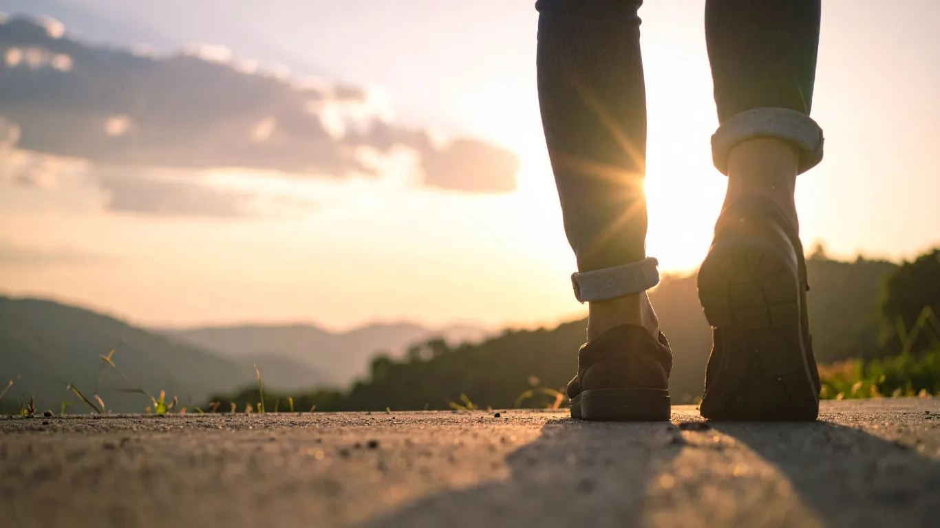 A person walking down a path toward the sunrise